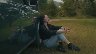 Taşralı bir kadın kırsal bir yolda bozuk bir eski arabanın yanında oturuyor. 