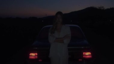 Sinematik çekim, kırmızı ışığı olan eski bir arabanın yanında duran bir kız. 