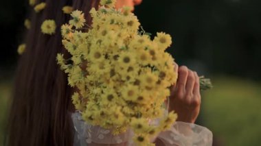 Güzel bir kadın neşeli sarı çiçeklerden oluşan bir buket tutuyor, doğadaki huzurlu bir anı yakalıyor.