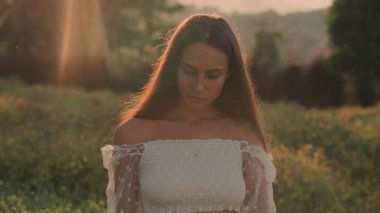 Zarif bir elbise giymiş bir kadın gün batımında canlı ve canlı tarlalarda zarifçe yürür.