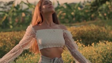 Göz kamaştırıcı bir kadın canlı sarı çiçeklerin arasında duruyor, dingin ve büyüleyici bir atmosfer yaratıyor.