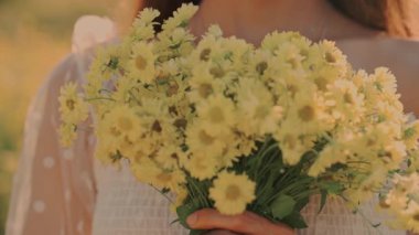 Güzel bir kadın neşeli sarı çiçeklerden oluşan bir buket tutuyor, doğadaki huzurlu bir anı yakalıyor.