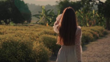 Zarif bir elbise giymiş bir kadın gün batımında canlı ve canlı tarlalarda zarifçe yürür.