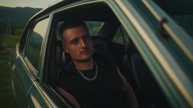 Kendine güvenen genç bir adam, nefes kesen doğal bir arka planla çevrili klasik bir arabada poz veriyor.