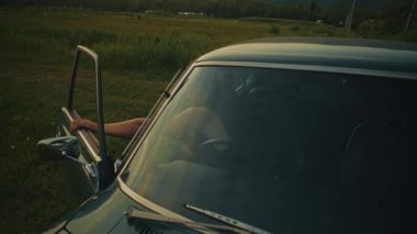 Bir akşam çekimi, klasik bir arabanın yanında duran bir adamı, huzurlu ve huzurlu bir alan ortamında yakalar.