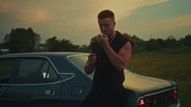 Genç bir adam klasik bir arabanın yanında günbatımında sakin ve huzurlu bir anı yakalıyor.