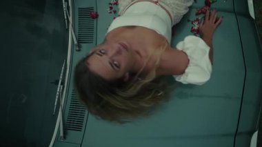 Zarif bir şekilde çiçekli taç yapraklarıyla süslenmiş bir arabada uzanan bir kadın derin ve zengin duygular taşıyor.