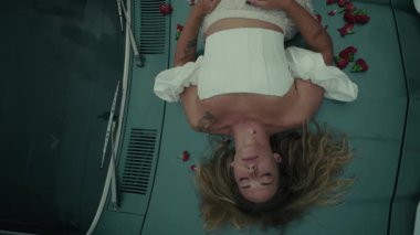 Zarif bir şekilde çiçekli taç yapraklarıyla süslenmiş bir arabada uzanan bir kadın derin ve zengin duygular taşıyor.