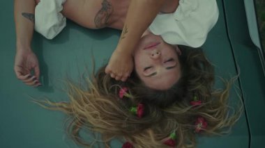 Zarif bir şekilde çiçekli taç yapraklarıyla süslenmiş bir arabada uzanan bir kadın derin ve zengin duygular taşıyor.