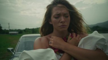 Yüzünde tedirgin bir ifade olan bir kadın dışarıda tek başına, sakin kırsal bir zemine karşı duygularıyla sarmalanmış bir şekilde duruyor.