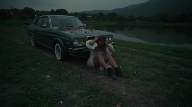 Huzurlu ve pitoresk bir sahne. Şafakta sakin bir gölün yanında, klasik bir arabanın yanında huzur içinde oturan bir kadın.