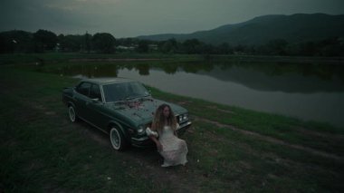 Renkli çiçeklerle bezenmiş eski bir arabanın yanında duran bir kadın, yakınlardaki dingin gölün yanında duyguları uyandırıyor.