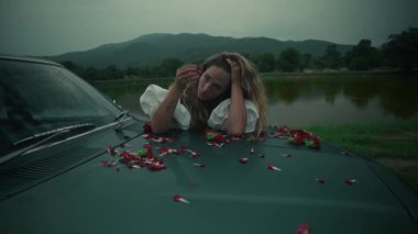 Sakin bir su gövdesinin taçyapraklarıyla süslenmiş arabada uzanan düşünceli bir kadını tasvir eden sakin bir sahne..