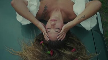 Zarif bir şekilde çiçekli taç yapraklarıyla süslenmiş bir arabada uzanan bir kadın derin ve zengin duygular taşıyor.