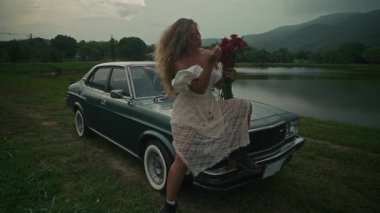 Resimli bir gölün yakınında, eski bir arabanın yanında canlı güller tutan bir kadınla huzurlu bir an.