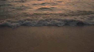 Okyanus dalgalarının dingin ve huzurlu güzelliğini hissedin. Renkli bir günbatımında yavaşça kıyıya vuruyor.