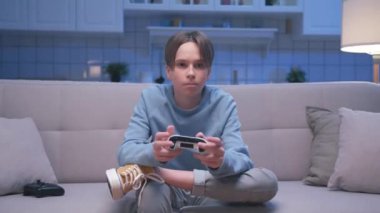 Bir genç çocuk video oyunu oynuyor ve modern kontrol mekanizması kullanıyor. Çocuk Ekrana Bakıyor ve Oyun Alanı Joystick 'i ile Eğleniyor. Livingroom 'da Genç Erkek Hobide Şans ve Zaferi Kaybediyor