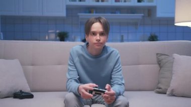 Bir genç çocuk video oyunu oynuyor ve modern kontrol mekanizması kullanıyor. Çocuk Ekrana Bakıyor ve Oyun Alanı Joystick 'i ile Eğleniyor. Livingroom 'da Genç Erkek Hobide Şans ve Zaferi Kaybediyor