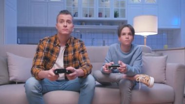 Action Oyuncuları Yetişkin Adam ve Guy Dijital Konsolda Oturuyor ve Video Oyunları Oynuyor. Video oyunu için joystickleri kontrol eden iki erkek oyuncu. Oturma odasında oyun oynamaya odaklanmak.