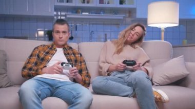 Action Oyuncuları Genç Adam ve Kadın Koltukta Oturuyor ve Dijital Konsolda Video Oyunları Oynuyor. Video oyunu için joystickleri kontrol eden iki oyuncu. Oturma odasında oyun oynamaya odaklanmış olmak.