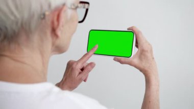 Yeşil Kroma Anahtarlı Yaşlı Kişi Dokunmatik Ekran Akıllı Telefonu. 50 'li yaşların kadın cep telefonunun tıkırdayan modeli. İzle ve İnternet Sosyal Medyasını Göster, Haberleri Oku, Uygulama E-Alışverişi