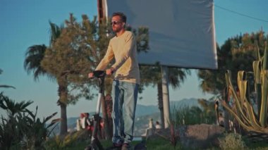 Man Riding Electric Tekme Scooter ve Sunset 'te İşe Taşınma. Geleneksel Trafikte Özgürlük İçin Geleceğin Moda Dengesi kavramı. Güneş Işığında Kiralık Kiralık Adam Tekmeleyicisinin Yeniden Yapımı