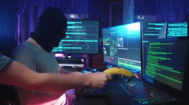 Masa 'daki Bilgisayar Programlama' da Korsan Kodlama ve Dinleme Müziği. Not Defterine Bakan ve Neon Renk Işığı 'ndaki Erkek Anonim Bilgisayar Korsanlığı. Hırsız Maskesi Sanal Veritabanını Hackledi