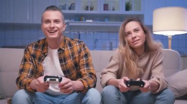 Action Oyuncuları Genç Adam ve Kadın Koltukta Oturuyor ve Dijital Konsolda Video Oyunları Oynuyor. Video oyunu için joystickleri kontrol eden iki oyuncu. Oturma odasında oyun oynamaya odaklanmış olmak.