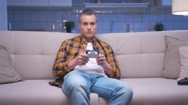 Koltukta oturan yakışıklı oyuncunun portresi ve dijital konsolda video oyunları oynaması. Tepki Erkek Oyuncu Video Oyunu için Joystick 'i kontrol ediyor. Bir kişi oturma odasında oyun oynamaya odaklanmış.