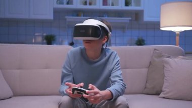 Kafkasyalı, VR kulaklık takan genç adam içeride video oyunu oynuyor. Kablosuz Medya Gözlüğü ve Konsol Kontrolörüyle Genç Çocuğun Yüzü 'nde Duygular. Sanal Gerçeklik için Dijital AR Gözlükleri