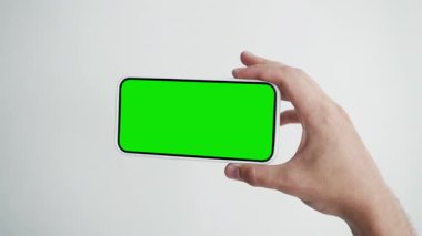 Genç adam, Yeşil Kroma Anahtarlı Ekran Akıllı Telefonu 'na bak. 30 'lu yaşlarda cep telefonu modeli üzerinde jest hareketi var. Konsept İzleme ve Gösterme İnternet Sosyal Medya, Çağrılar, Haber Oku, Uygulama, Çok, Film