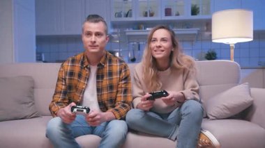 Action Gamer Genç Adam ve Kadın Koltukta Oturuyor ve Dijital Konsolda Video Oyunları Oynuyor. Video oyunu için oyun oynayan iki oyuncu joystickleri kontrol ediyor. Oyun ve Kazanma Konferans Odası 'na Odaklanmak