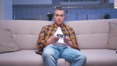 Koltukta oturan yakışıklı oyuncunun portresi ve dijital konsolda video oyunları oynaması. Tepki Erkek Oyuncu Video Oyunu için Joystick 'i kontrol ediyor. Bir kişi oturma odasında oyun oynamaya odaklanmış.