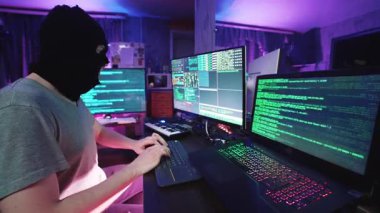 Masa 'daki Bilgisayar Programlama' da Korsan Kodlama ve Dinleme Müziği. Not Defterine Bakan ve Neon Renk Işığı 'ndaki Erkek Anonim Bilgisayar Korsanlığı. Hırsız Maskesi Sanal Veritabanını Hackledi