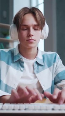 Kulaklıklı Genç Meşgul Çocuğun Portresi Bilgisayar Klavyesinde Ödev Yazıyor. Erkek Çocuk Okul Ofisinde Oturuyor ve Bilgisayarda Uzaktan Çalışma Yazıyor. Öğrenim Uzaklık Teknolojisi ve Kapalı Öğrenci Yaşamında Müzikal