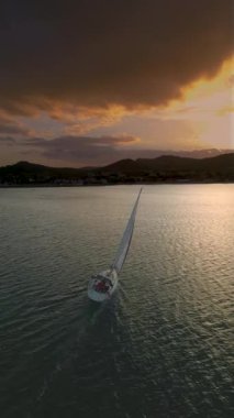 Gün batımında körfezdeki orta büyüklükteki yatın havadan görünüşü. Denizde romantik günbatımı. Gün batımında açık denizde yelken açacağız. Havadan 4K video görüntüsü alıyoruz. Yüksek kalite 4k görüntü