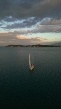 Gün batımında körfezdeki orta büyüklükteki yatın havadan görünüşü. Denizde romantik günbatımı. Gün batımında açık denizde yelken açacağız. Havadan 4K video görüntüsü alıyoruz. Yüksek kalite 4k görüntü