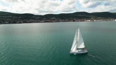 Aerial of sun yacht sail in agean sea. White boat at open sea. Summer cruise on sailboat at sunlight with clouds. urla izmir sea coast with water transport. . High quality 4k footage