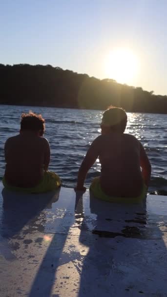 Widok Tyłu Dwójki Dzieci Siedzących Strojach Kąpielowych Molo Zachodzie Słońca — Wideo stockowe