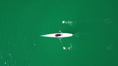 Aerial drone birds eye view video of sport canoe operated by young woman in emerald clear waters. High quality 4k footage