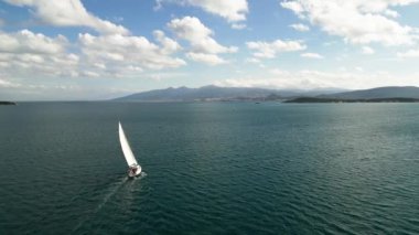 Güneş yatının havası yaşlılık denizinde yüzüyor. Açık denizde beyaz tekne. Güneş ışığında bulutlu bir yelkenliyle yaz gezisi. Urla izmir deniz kıyısı ve su taşımacılığı. - Evet. Yüksek kalite 4k görüntü