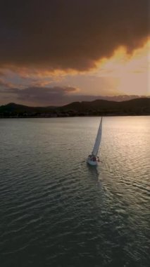 Gün batımında körfezdeki orta büyüklükteki yatın havadan görünüşü. Denizde romantik günbatımı. Gün batımında açık denizde yelken açacağız. Havadan 4K video görüntüsü alıyoruz. Yüksek kalite 4k görüntü