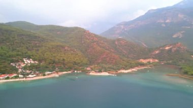 Fethiye 'deki Oludeniz yarımadasının muhteşem hava manzarası, mavi lagün, kumlu sahil üzerinde İHA uçuşu, turkuaz deniz, güneş yatakları ve şemsiyeli sahil beldesi, sıcak yaz günü. Yüksek kalite 4k görüntü