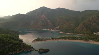 Fethiye 'deki Oludeniz yarımadasının muhteşem hava manzarası, mavi lagün, kumlu sahil üzerinde İHA uçuşu, turkuaz deniz, güneş yatakları ve şemsiyeli sahil beldesi, sıcak yaz günü. Yüksek kalite 4k görüntü