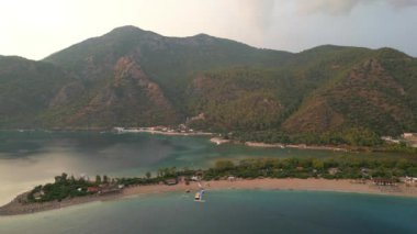 Fethiye 'deki Oludeniz yarımadasının muhteşem hava manzarası, mavi lagün, kumlu sahil üzerinde İHA uçuşu, turkuaz deniz, güneş yatakları ve şemsiyeli sahil beldesi, sıcak yaz günü. Yüksek kalite 4k görüntü