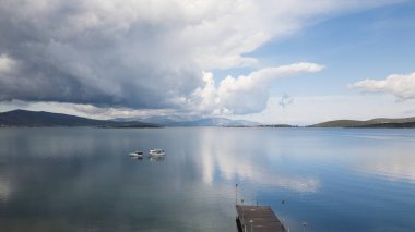 Önünde bir rıhtım bulunan doğal bir manzara, suyla çevrili ve bulutlu bir gökyüzü, arka planda kümülüs bulutları, pitoresk bir ufuk oluşturuyor.