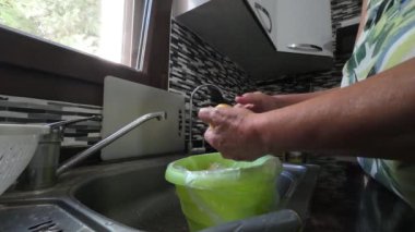 Bir kadın eli mutfak lavabosunun üzerinde patates soyarken mutfakta yemek pişirmek için sebze soyuyordu. Musluktan su akar. Yüksek kalite 4k görüntü
