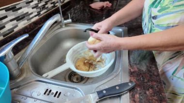 Bir kadın eli mutfak lavabosunun üzerinde patates soyarken mutfakta yemek pişirmek için sebze soyuyordu. Musluktan su akar. Yüksek kalite 4k görüntü