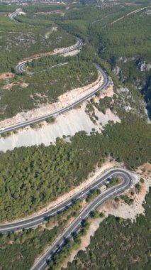 Türkiye 'nin Marmaris kenti yakınlarındaki ağaçlar arasındaki dolambaçlı dağ yolunun üzerinde havadan atılan bir hava aracı. Yaz sonu hava bulutlu. 4K virajında araba sürüyor. Dümdüz uçuyor. Yüksek kalite 4k