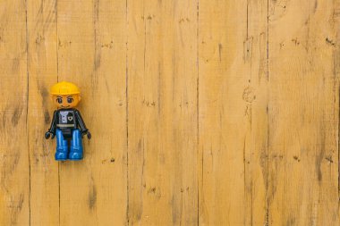 Lego inşaat işçisi figürü mavi botlar ve ahşap arka planda sarı kask.